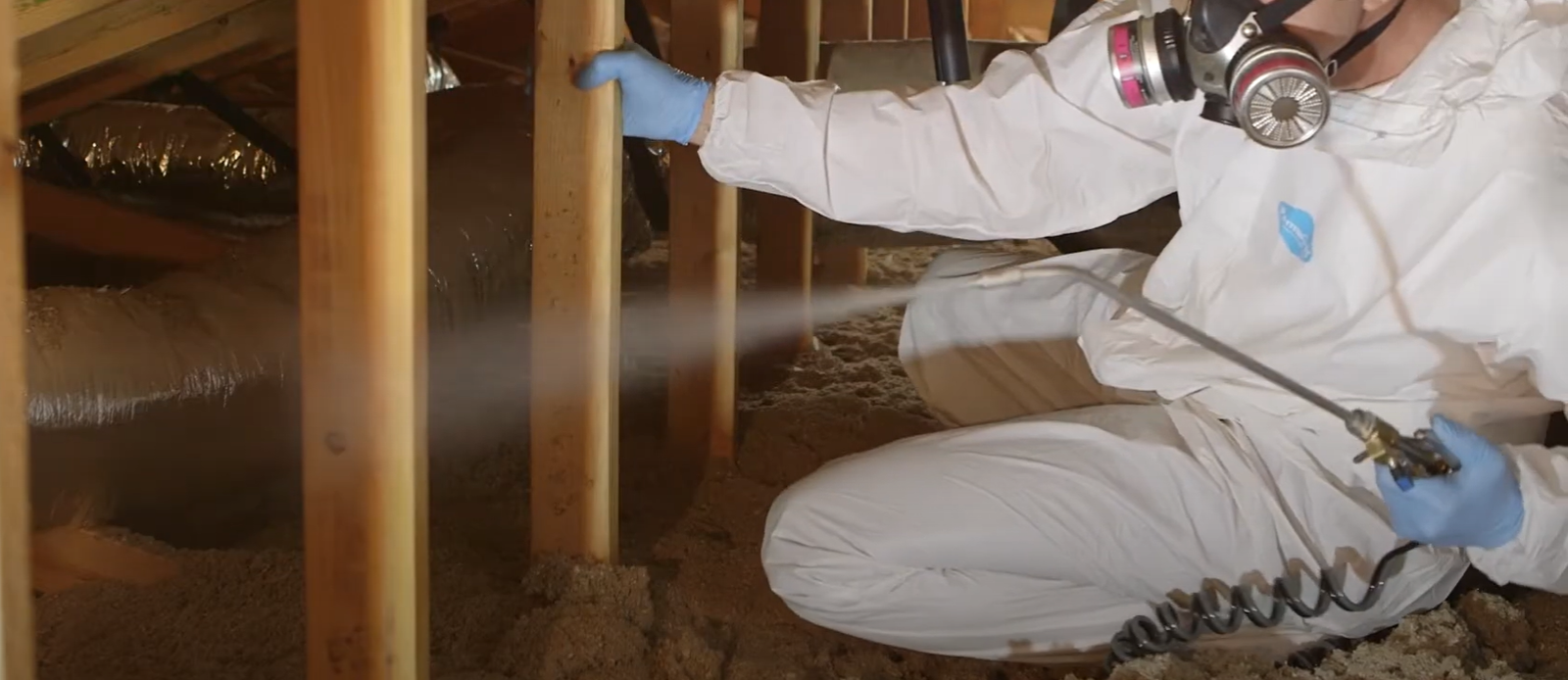 A pest control technician in protective gear spraying inside an attic – Rodent Control in Baltimore.