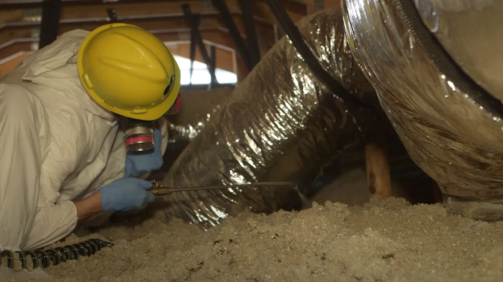 A pest control technician in protective gear spraying inside an attic – Rodent Control in Baltimore.